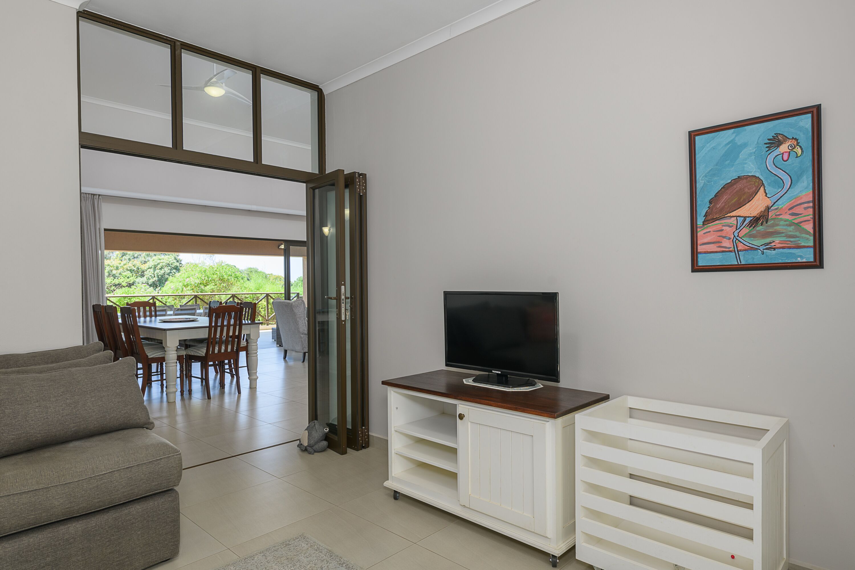 Uma sala de estar com sofá, televisão sobre suporte de madeira, e um espaço de refeições com cadeiras e mesa.