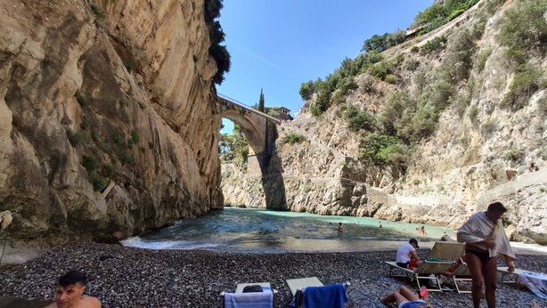 Une plage rocheuse avec un pont, des gens qui se détendent et une piscine.