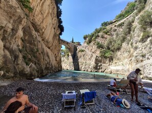 A rocky beach with a bridge, people relaxing, and a pool. - Casa Vacanze Angelica (Salerno)