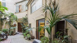 Une petite cour intérieure agrémentée de plantes en pot, avec une moto et l’entrée d’un immeuble.