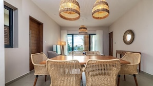 Ein Essbereich mit einem großen Holztisch, umgeben von Korbstühlen, mit hängenden Pendelleuchten aus Korb und Blick durch große Fenster.