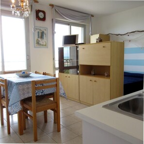 Een keuken met een eettafel, stoelen, een kroonluchter, een klok en uitzicht door het raam.