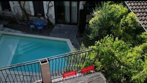 Una terraza de madera con piscina, sillas rojas y una mesa.
