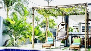A poolside area with a hanging chair, a cushioned chair, and a small table. - Nubian Villa-A Tropical Gem with Pool and Hot Tub (Adenta Municipality)