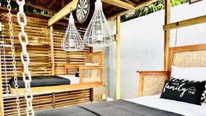 A cozy outdoor bedroom with a hammock, a bed with a black quilt, and a wicker headboard. - Nubian Villa-A Tropical Gem with Pool and Hot Tub (Adenta Municipality)