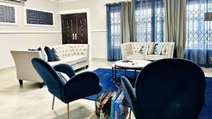 A modern living room with a beige sofa, blue armchairs, a coffee table, and a bookshelf. - Nubian Villa-A Tropical Gem with Pool and Hot Tub (Adenta Municipality)