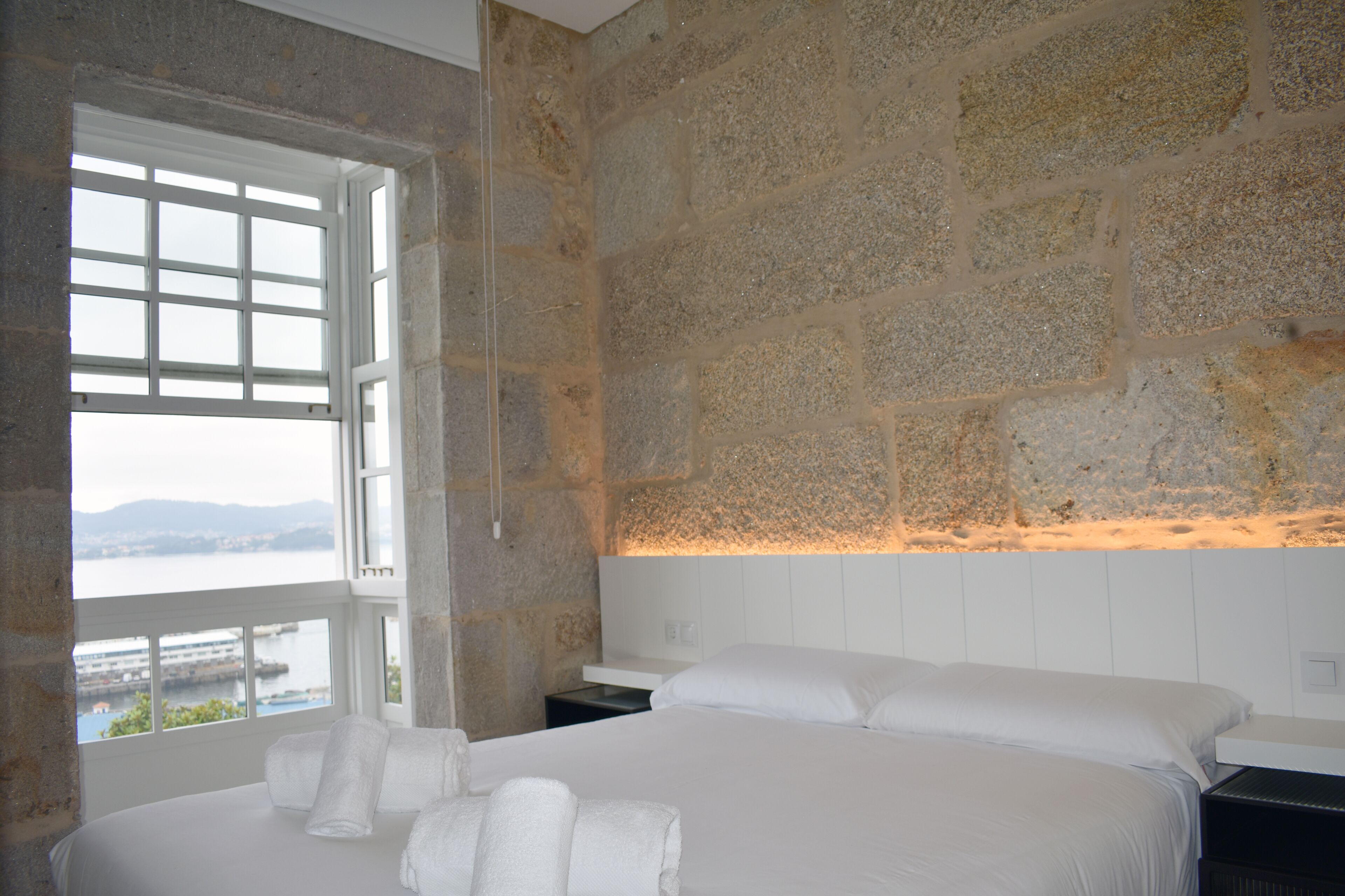 Una habitación de hotel con una cama grande, una pared de piedra y una ventana con vistas al agua.