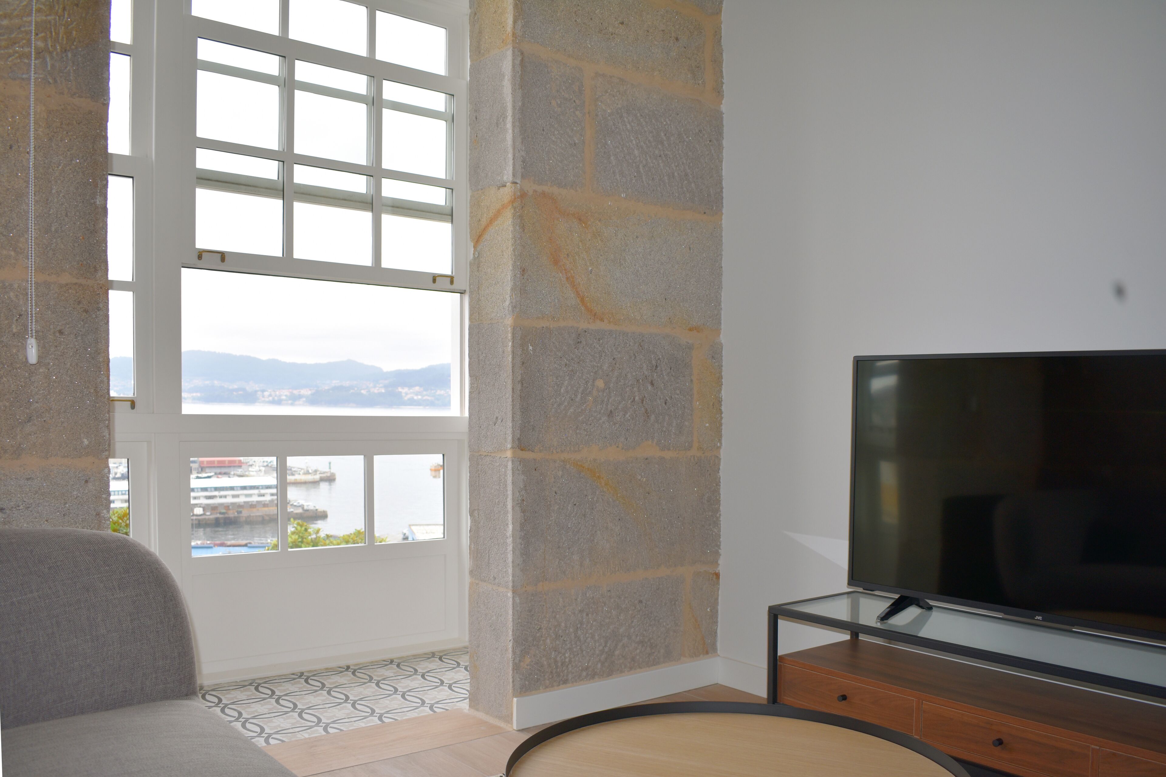 Una habitación con un ventanal grande, un televisor sobre un mueble de madera y un suelo estampado.