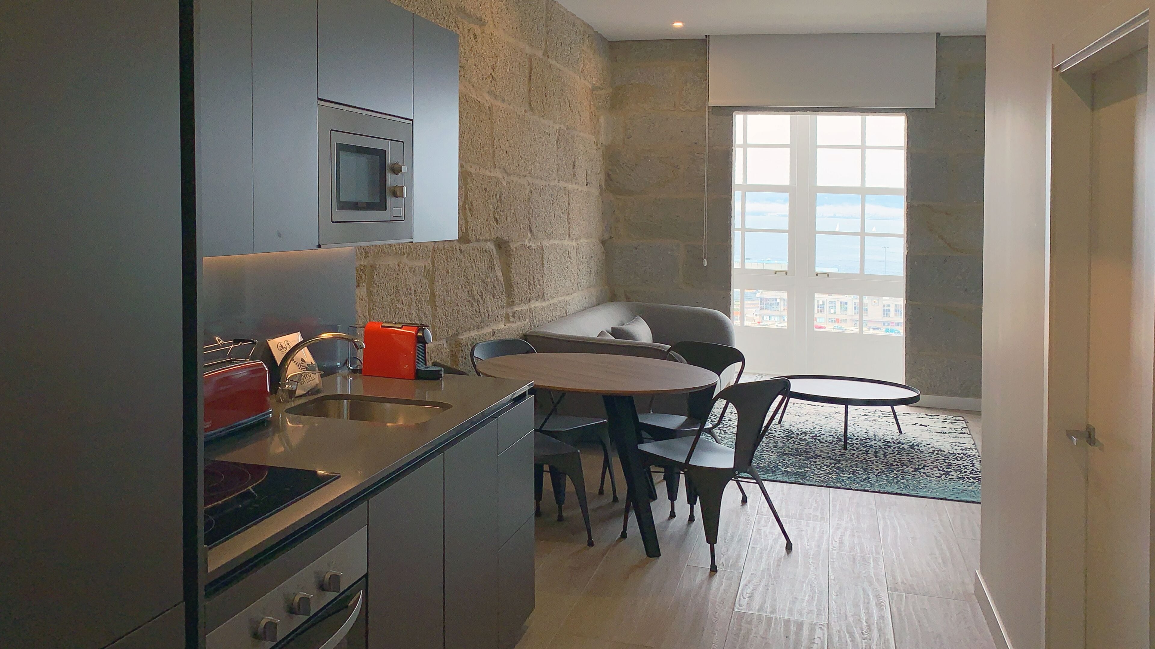 A modern kitchen with a stone wall, a built-in oven, and a dining area with a round table and chairs.