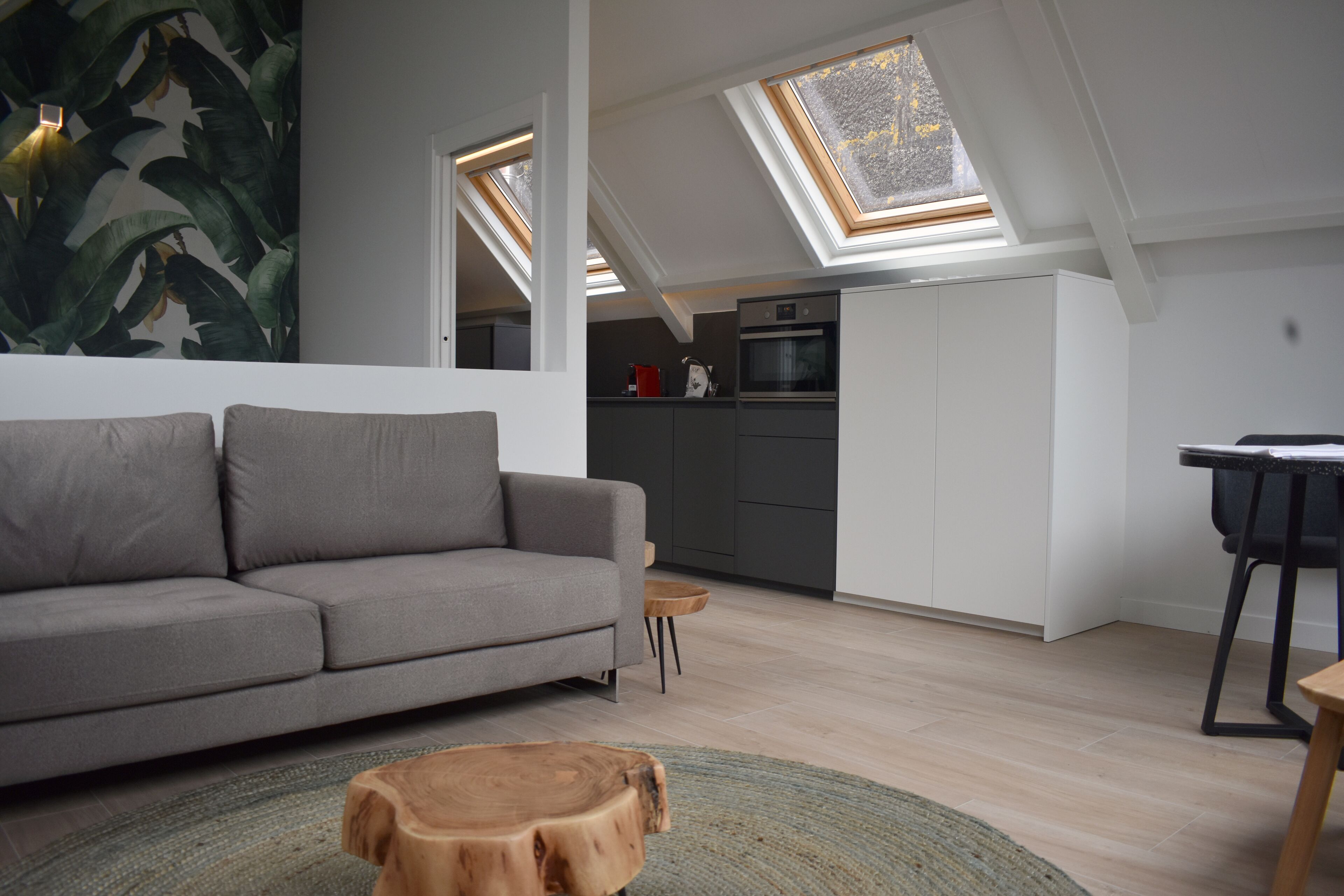 A modern loft apartment with a grey sofa, wooden coffee table, skylights, and a kitchen area.