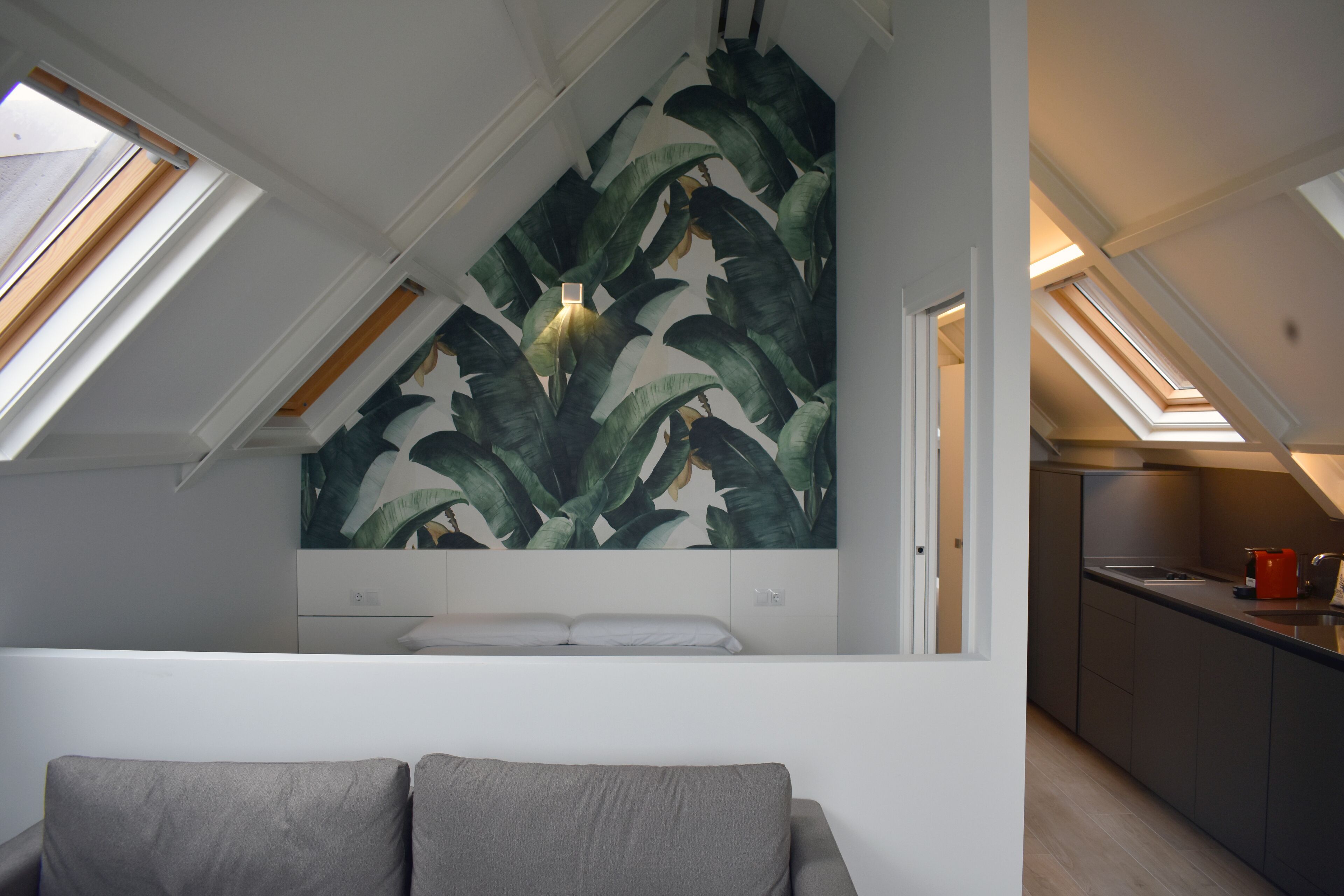 Un dormitorio tipo loft moderno con tragaluces, un mural botánico grande y una kitchenette.