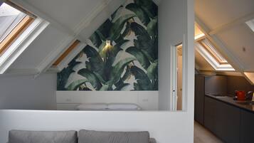 Un dormitorio tipo loft moderno con tragaluces, un mural botánico grande y una kitchenette.