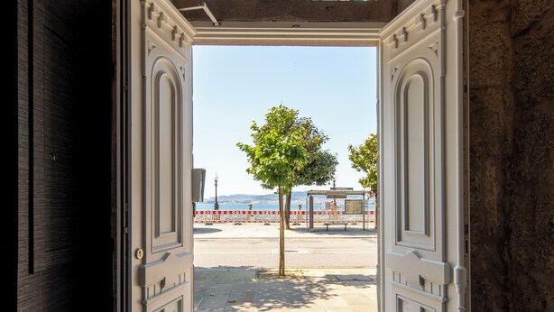 An open doorway leading to a paved area with a tree and a view of the sea. - Bow Homes by Como en Casa (Vigo)