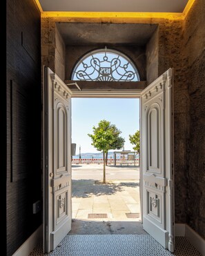 An open doorway leading to a paved area with a tree and a view of the sea. - Bow Homes by Como en Casa (Vigo)