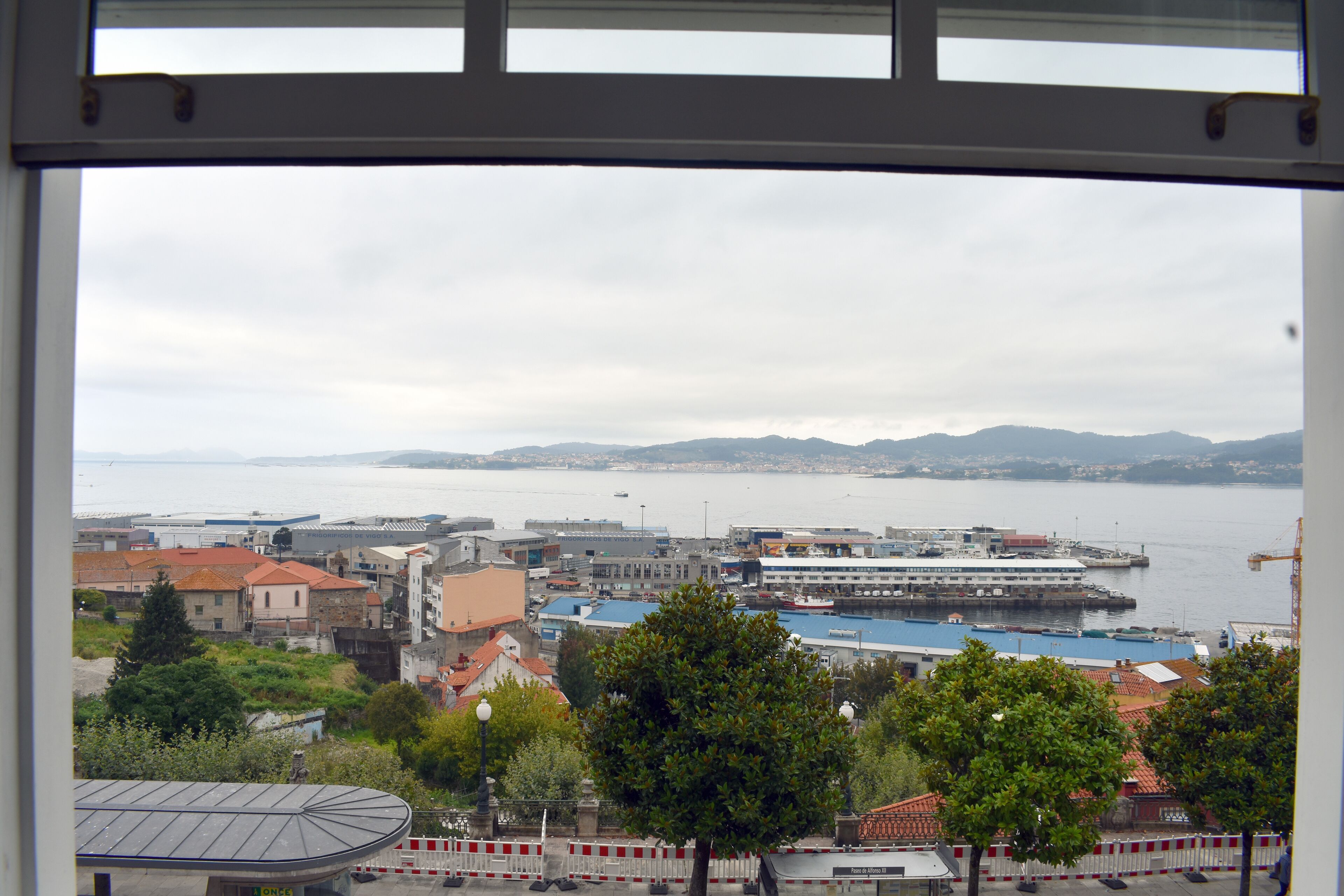 Vista de un paisaje costero con edificios, un puerto y montañas a lo lejos.