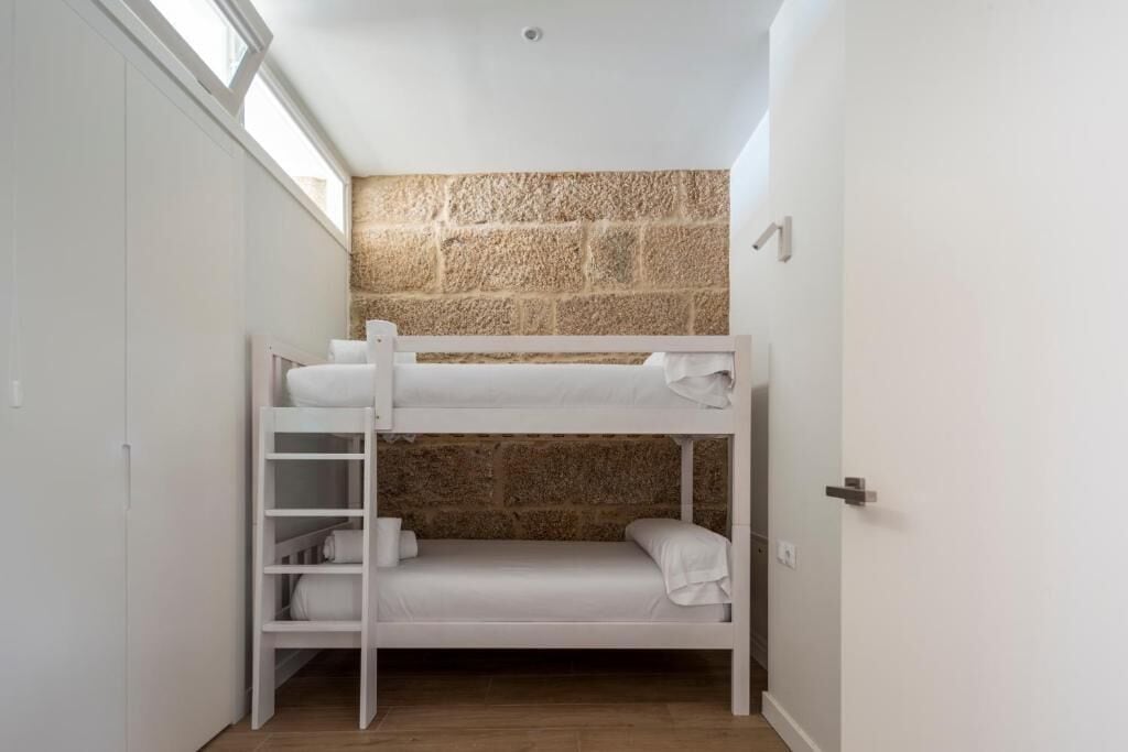 A bunk bed in a small room with a stone wall and a window.