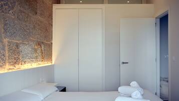A hotel room with a large bed, a stone wall, and a wardrobe.