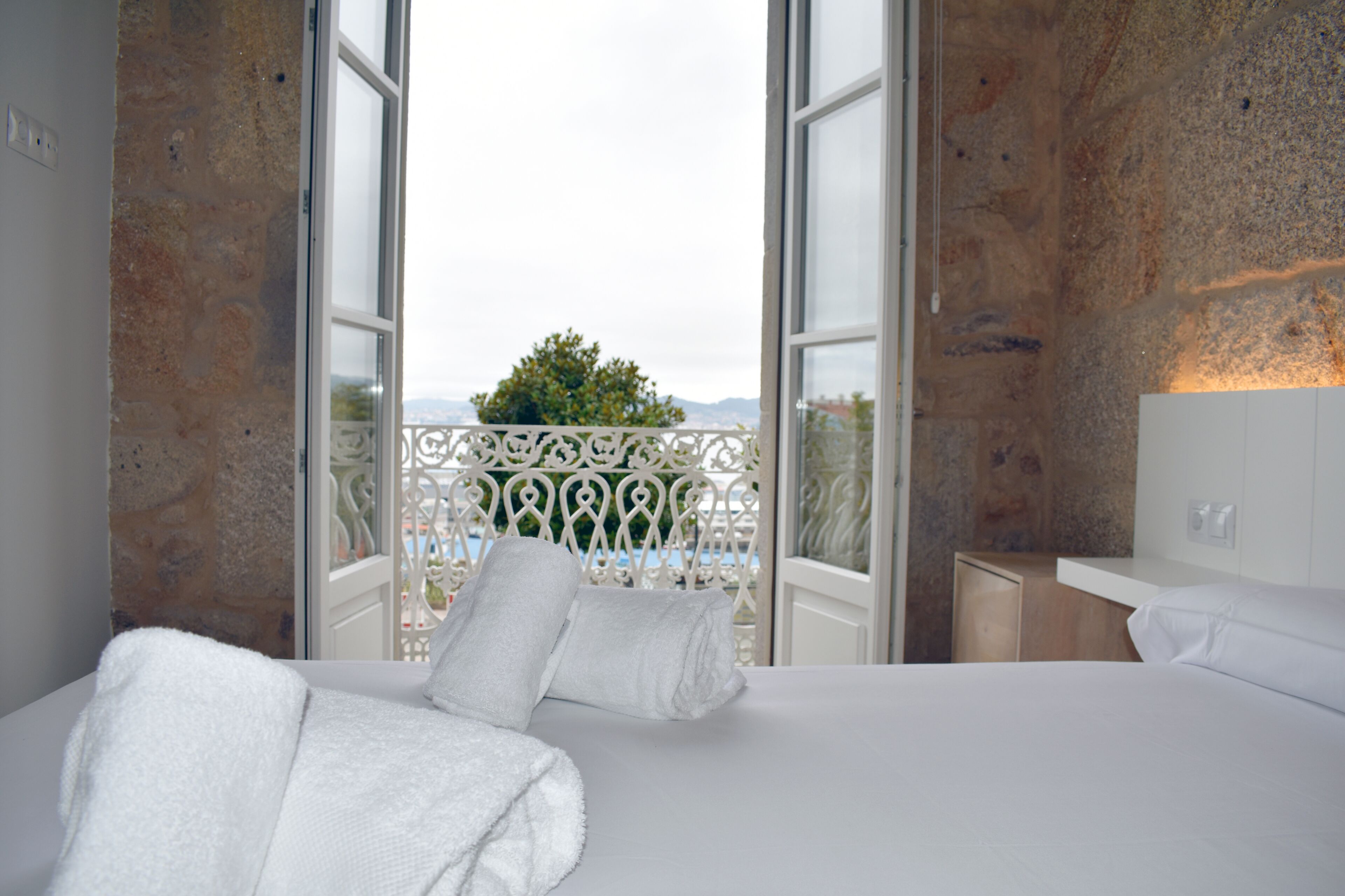 A hotel room with a bed, a nightstand, and a view of a balcony with a railing.