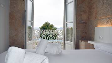 A hotel room with a bed, a nightstand, and a view of a balcony with a railing.