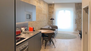 A modern kitchen with grey cabinets, a red toaster, and a sink. There is a dining area with a table and chairs, and a sofa in the background. - Bow Homes by Como en Casa (Vigo)