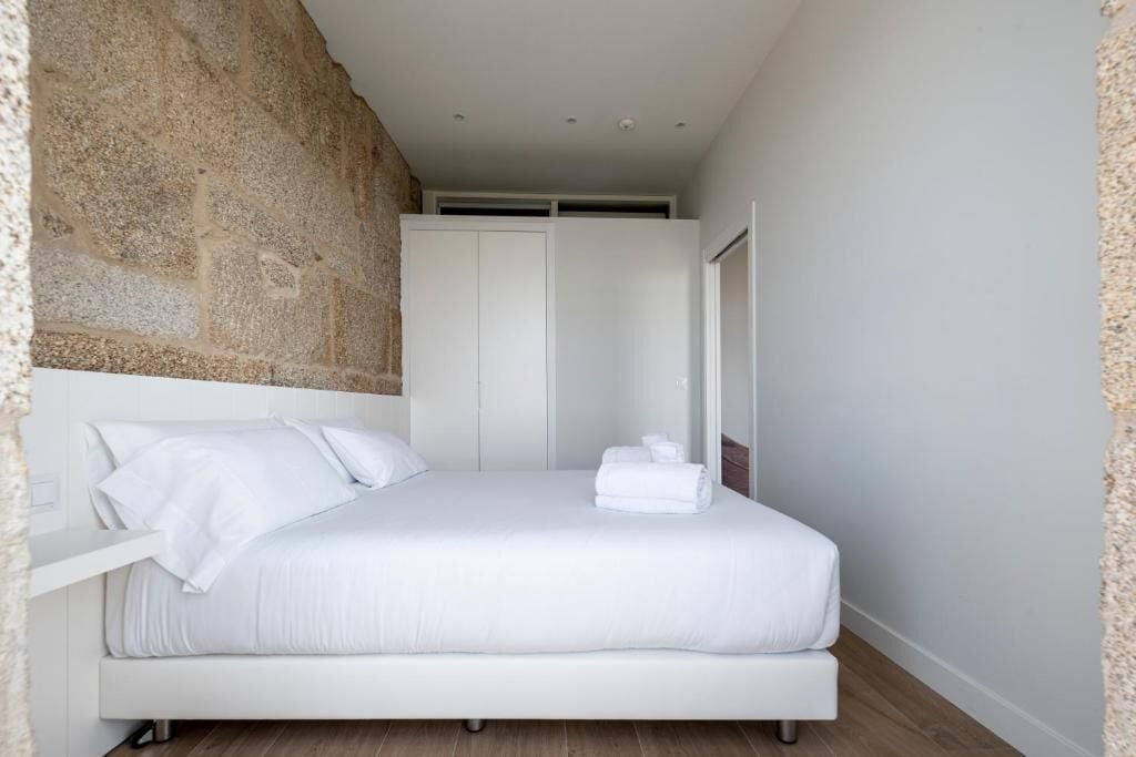 Une chambre moderne avec un grand lit, des murs blancs et un mur d’accent en pierre.