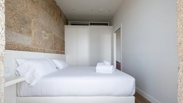 Une chambre moderne avec un grand lit, des murs blancs et un mur d’accent en pierre.