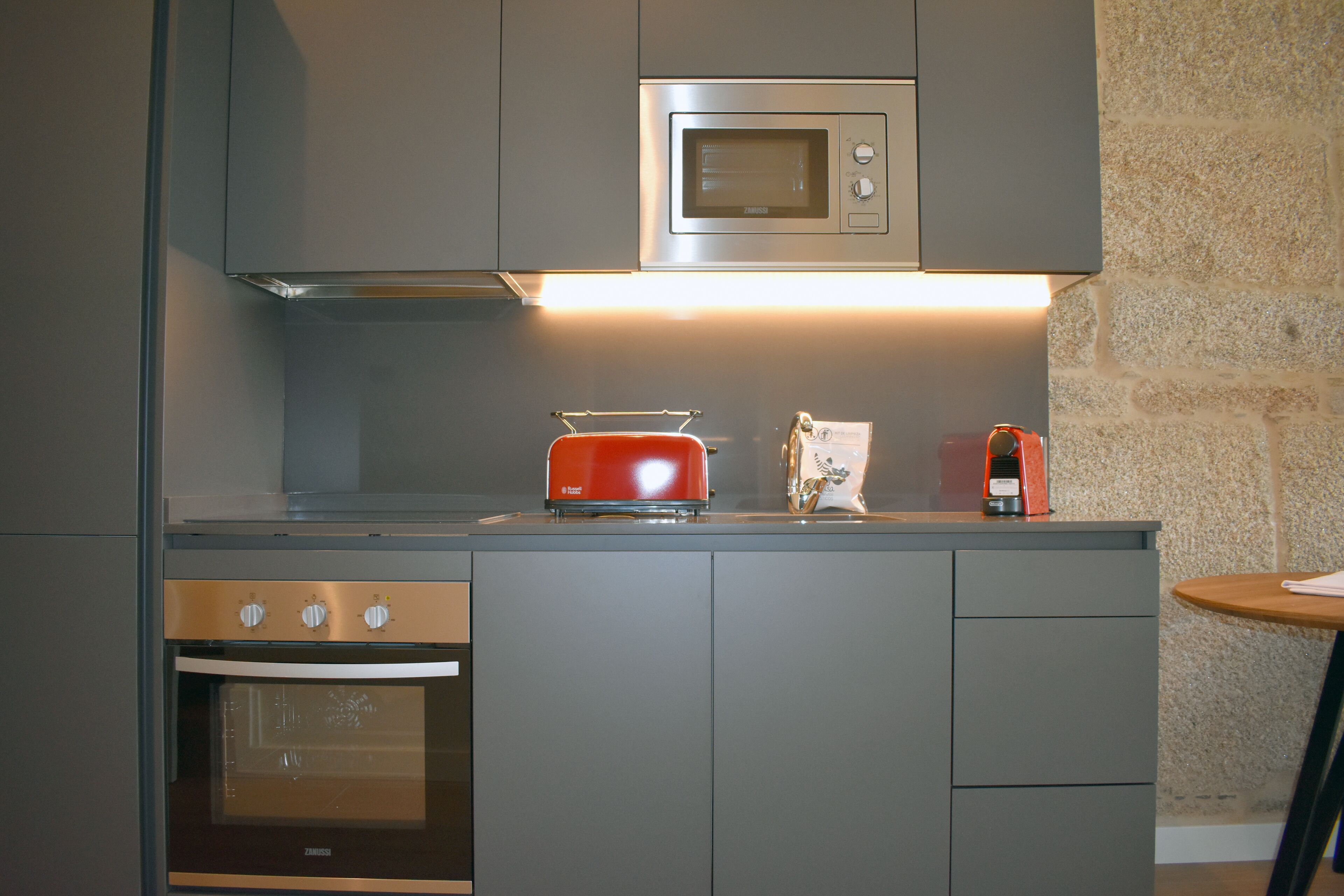 Una cocina moderna con horno empotrado, microondas y tostadora roja.