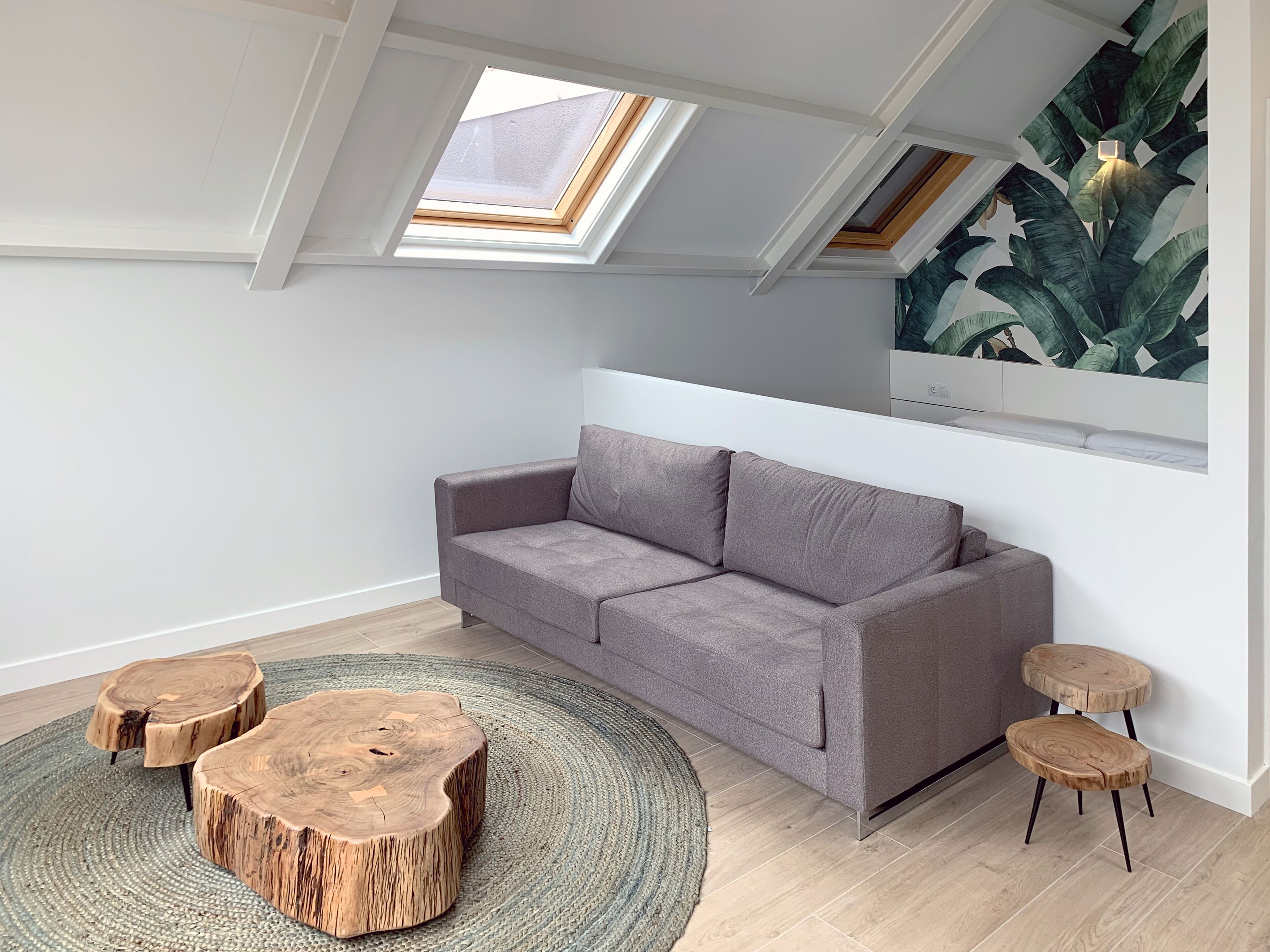 A modern living room with a grey sofa, wooden round tables, and a large window with a view of a plant.