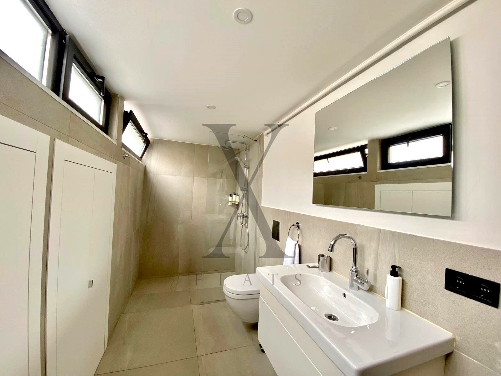 A modern bathroom with a large sink, mirror, and shower.