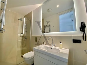 A modern bathroom with a glass-enclosed shower, a white sink with a mirror above it, and a toilet. - X Flats Taksim (Istanbul)