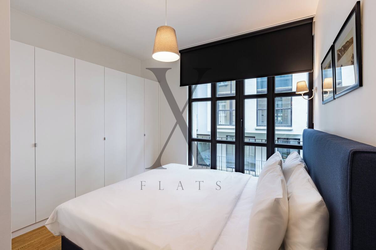A modern bedroom with a large bed, a window with a view of buildings, and a wardrobe.