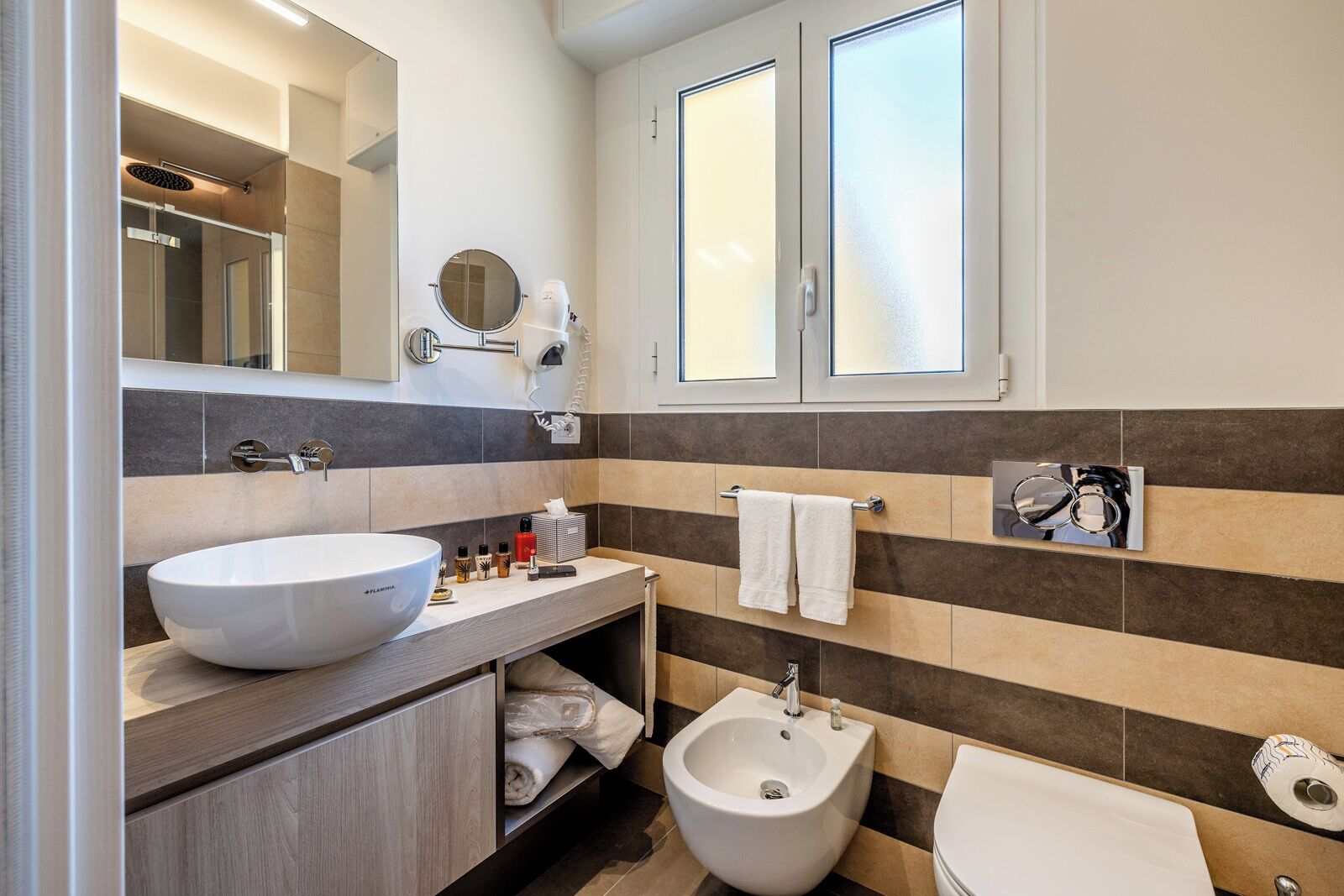 Un baño moderno con un lavamanos de pedestal, un bidé, un inodoro y un espejo con toallero.