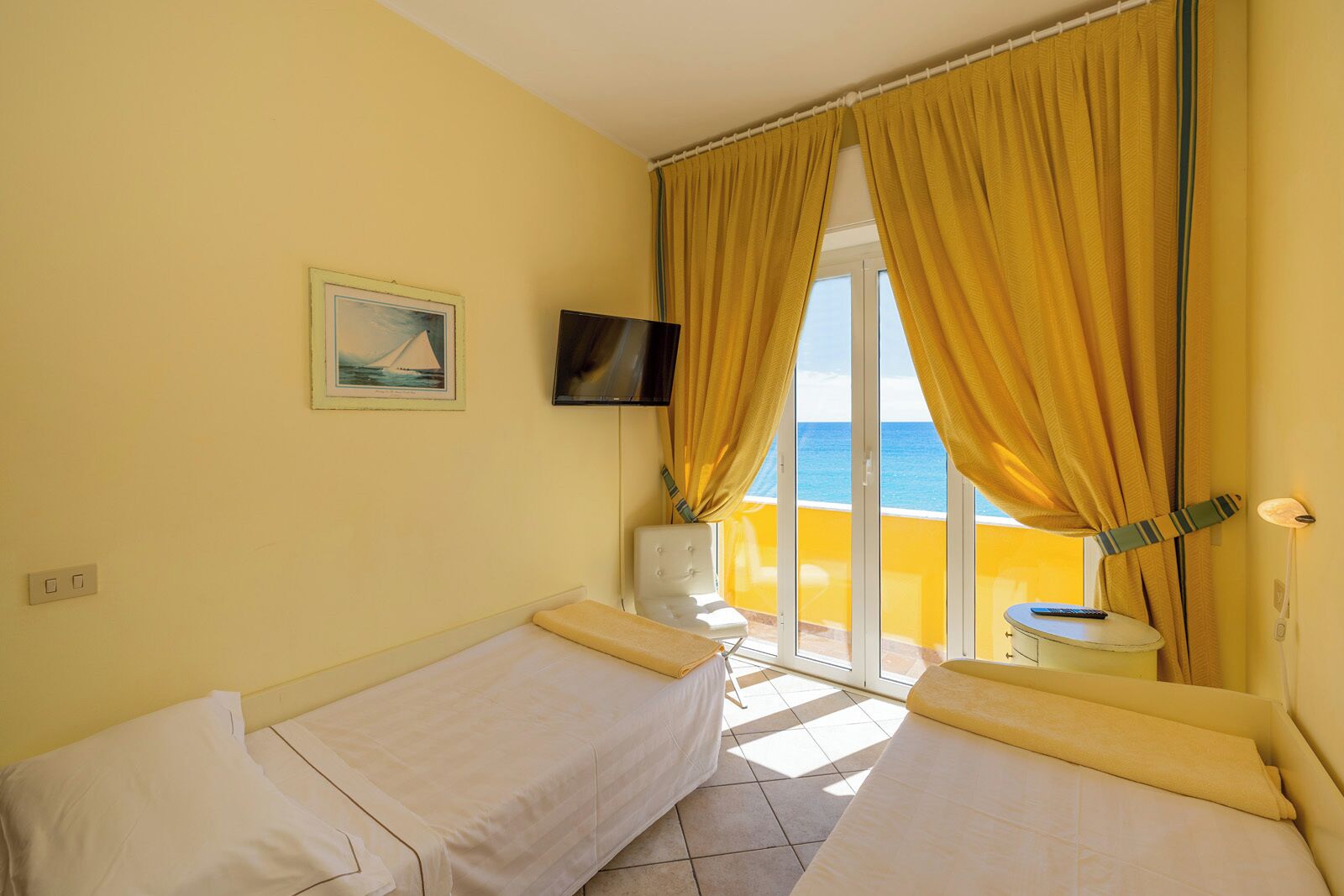Une chambre avec deux lits, une télévision, un tableau et une vue sur la mer.