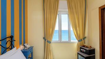 A hotel room with a bed, a bedside table with a phone, a small fridge, and a window with curtains.