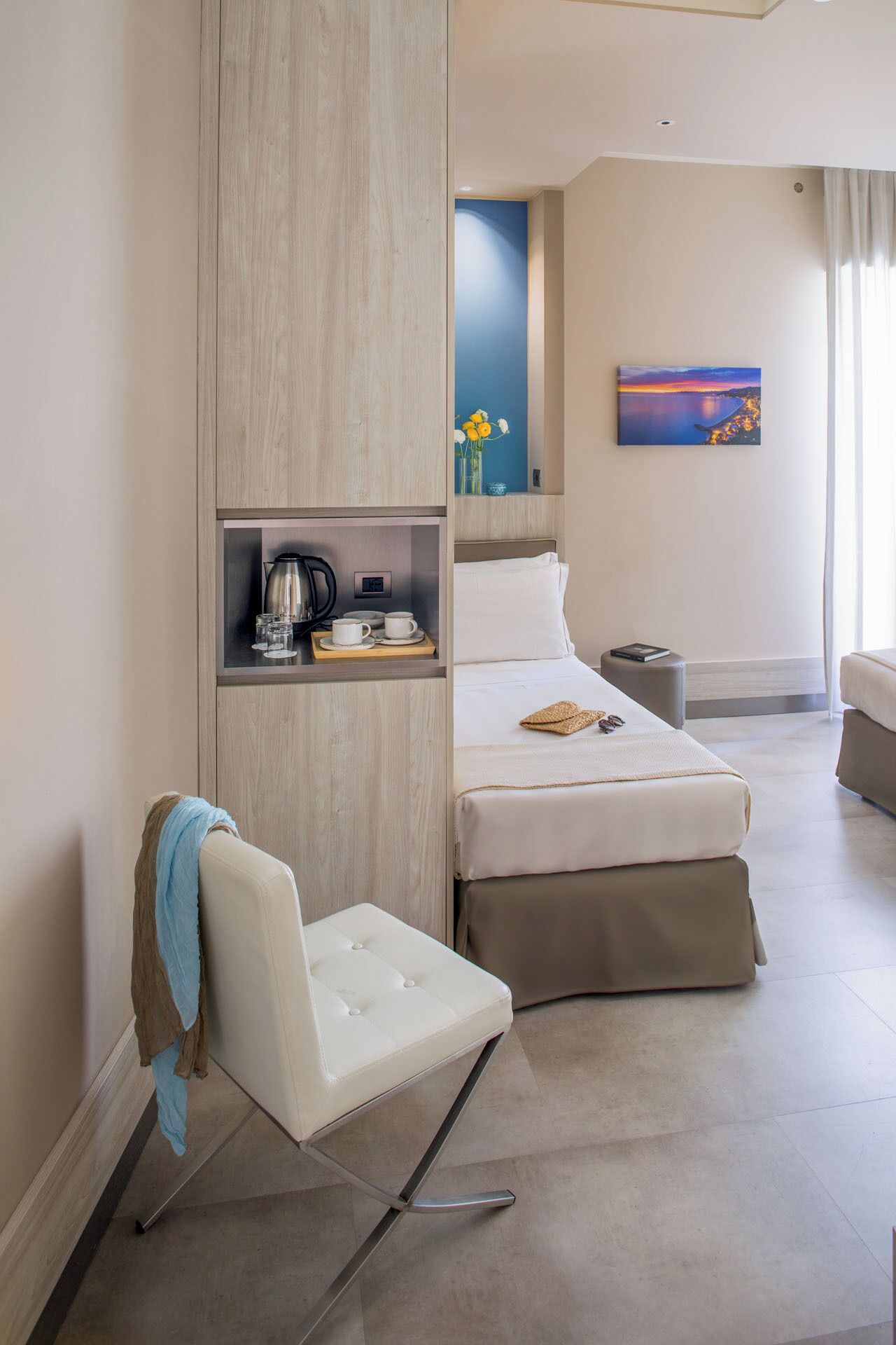 A modern hotel room with a bed, a seating area, a coffee station, and a painting on the wall.