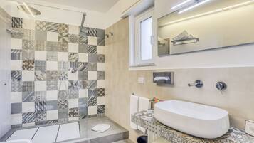 Ein modernes Badezimmer mit einer großen Badewanne, einer Dusche mit gemusterten Fliesen und einem Spiegel über dem Waschbecken.