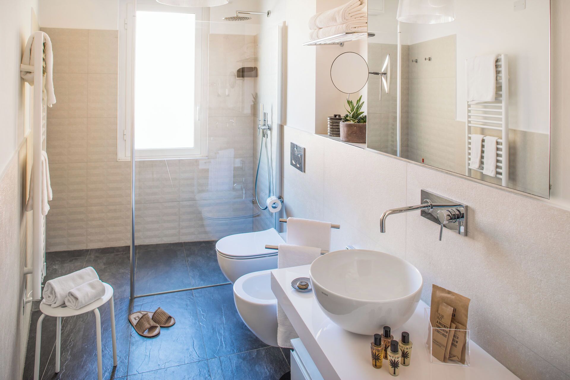 Une salle de bain moderne avec une douche à parois de verre, des toilettes, un lavabo avec un grand bac et un miroir.