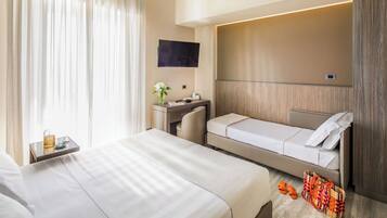 Quarto de hotel com duas camas, uma escrivaninha, televisão e janela com cortinas.