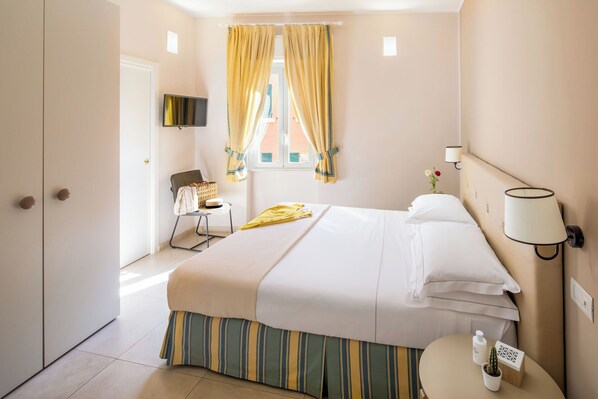 A hotel room with a bed, a chair, a TV, a window with curtains, a bedside lamp, and a small table with a cactus.