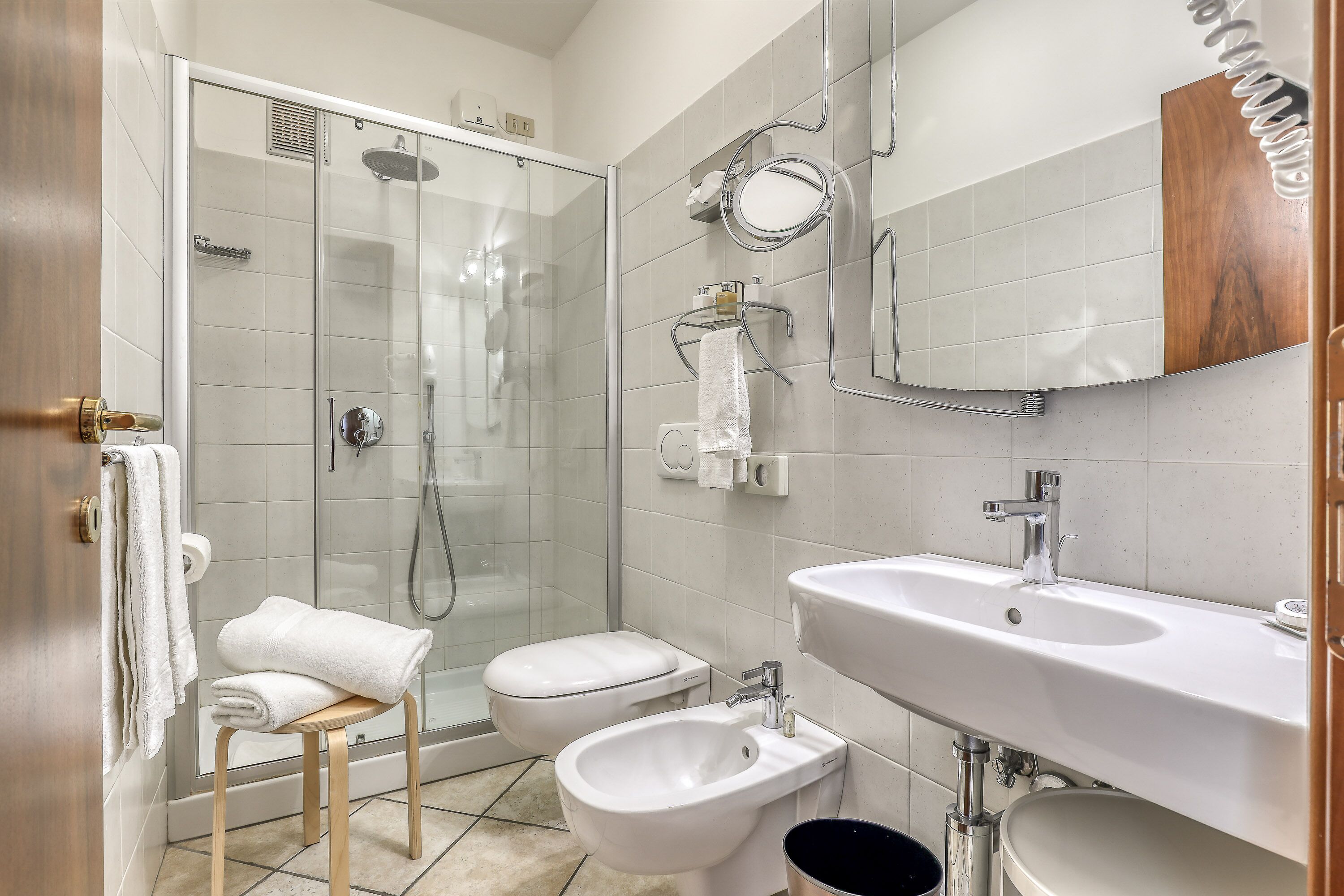 A modern bathroom with a glass-enclosed shower, a toilet, a bidet, and a sink with a mirror above.