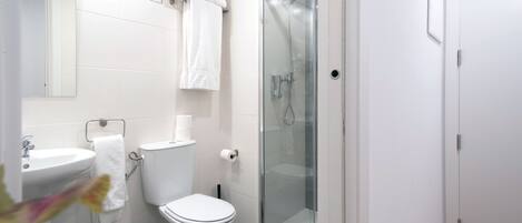 Un baño moderno con ducha de vidrio, inodoro blanco y lavamanos.