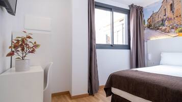Una habitación de hotel con una cama, un escritorio con una planta, una ventana con cortinas y un mural en la pared.