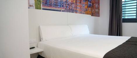 Habitación de hotel con una cama grande, una mesita de noche, un cuadro de un paisaje urbano y una ventana con cortinas.