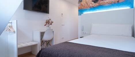 A bedroom with a bed, a desk, a chair, a TV, and a painting of a coastal landscape.