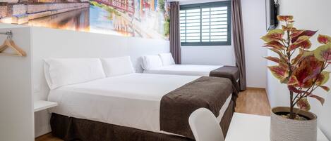 Habitación de hotel con dos camas, un escritorio, una planta en maceta, un mural y una ventana con cortinas.