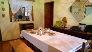 Un coin repas avec une table dressée pour deux personnes, un banc et une fenêtre avec des rideaux.
