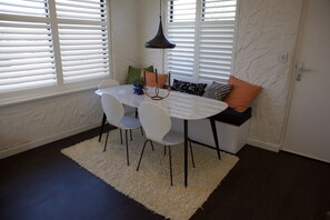 A dining area with a white table, four white chairs, a black pendant light, and a white shag rug. - Luxurious unit by the Beach (Glenelg South)