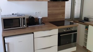 Une cuisine compacte équipée d’un four à micro-ondes, d’un grille-pain, d’un réfrigérateur, d’un four et d’un grand téléviseur fixé au mur.