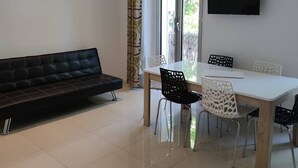 Un salon moderne avec un canapé, une table à manger, des chaises et un téléviseur fixé au mur.