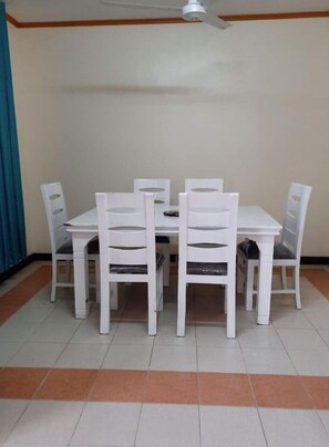 A dining area with a white table and chairs, a ceiling fan, and a tiled floor with a brown border.
